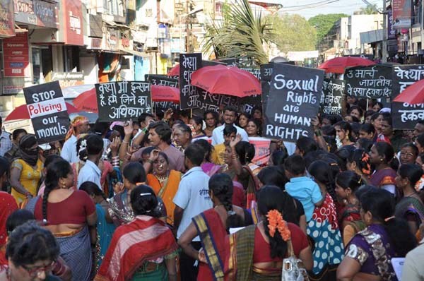 A protest by sex workers. They are wearing sarees, holding red umbrellas, and placards reading "Stop policing our morals", "Sexual rights are human rights".