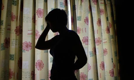 Silhouette of a short-haired woman standing in a room. Light enters through curtains on a window.