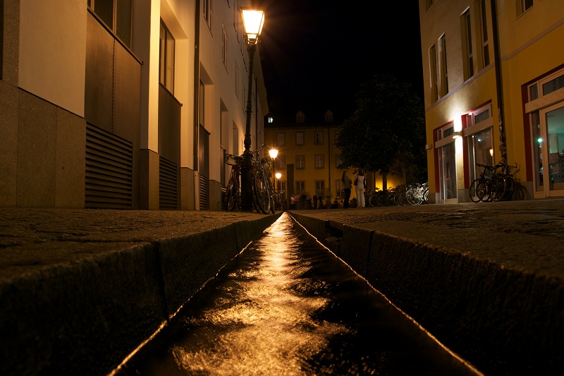Photo of a street at night time. There are houses on both the sides, and street lights are on.