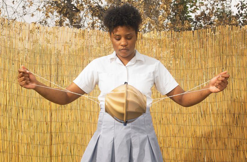 A brown girl is holding the Flo toolkit that supports girls living in poverty to wash, dry and carry reusable sanitary pads. It has a ball-type shape in the middle, and a string on both ends. The girl is stretching the string as if to give the central part a spin.