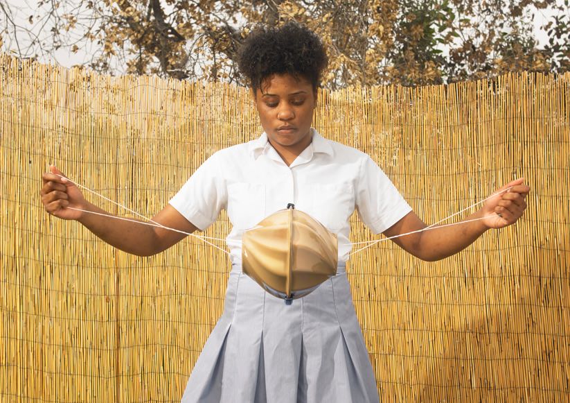 A brown girl is holding the Flo toolkit that supports girls living in poverty to wash, dry and carry reusable sanitary pads. It has a ball-type shape in the middle, and a string on both ends. The girl is stretching the string as if to give the central part a spin.