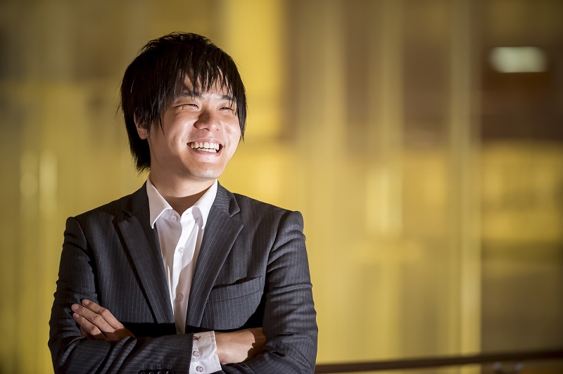 Rath Wang in professional attire of white shirt and black coat. His hands are crossed, and he is smiling. The image is from the torso up.