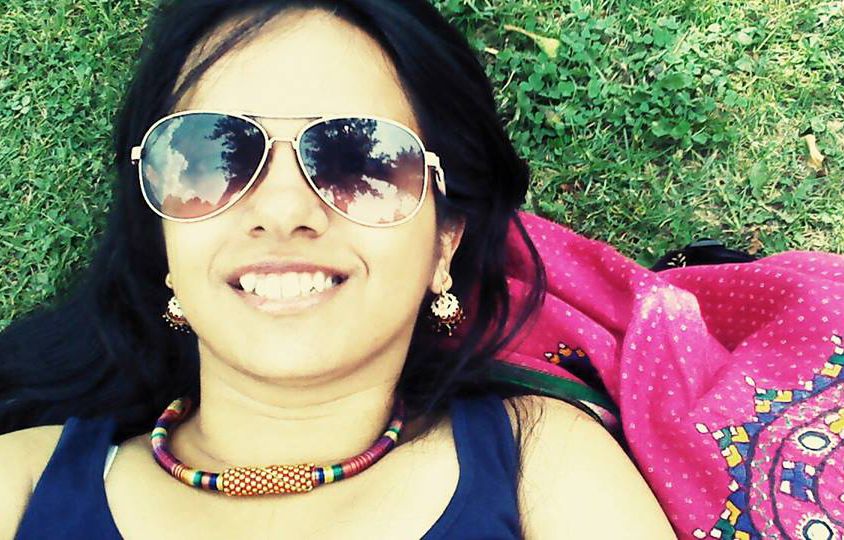 Feminism in India founder Japleen Pasricha lying under the sun on grass. She is smiling, wearing goggles, earrings, necklace, and a tank top.