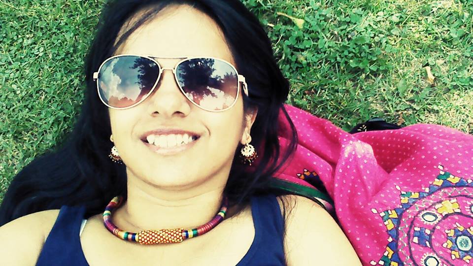 Feminism in India founder Japleen Pasricha lying under the sun on grass. She is smiling, wearing goggles, earrings, necklace, and a tank top.