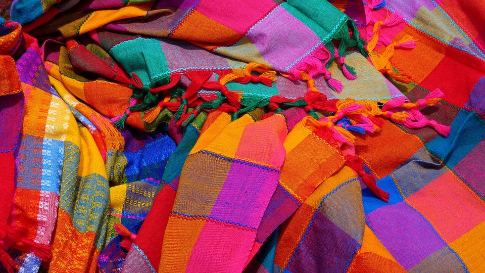 Bright, goddy-coloured shawls lying in a messy, scattered way. Screen reader support enabled. Bright, goddy-coloured shawls lying in a messy, scattered way.