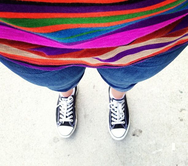 Selfie by a woman showing her striped, bright-coloured top, blue capri, and black and white sneakers.