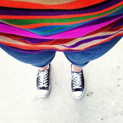 Selfie by a woman showing her striped, bright-coloured top, blue capri, and black and white sneakers.