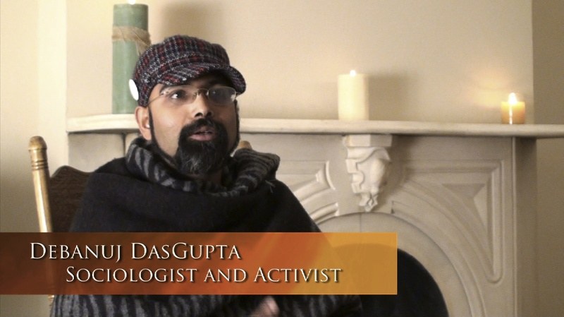 Debanuj Dasgupta sitting on a chair, speaking something. On bottom left of photo is written his name and designation "socialist and activist".