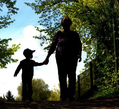 A woman walking, holding hands with her preschooler son in a garden.