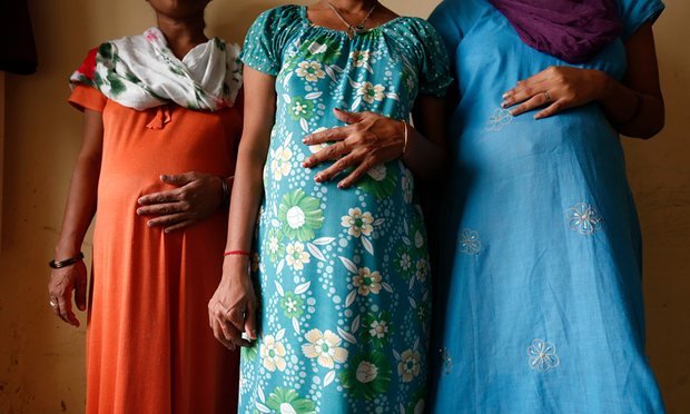 Photo of three Indian pregnant women from neck to knee with each resting their right hands on their protruding belly. One is wearin suit, and two are wearing night gown.