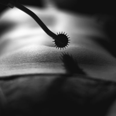 Kink. A rod with a round-shaped end with spikes coming out of it held near a nude woman's navel by someone not visible in the picture.