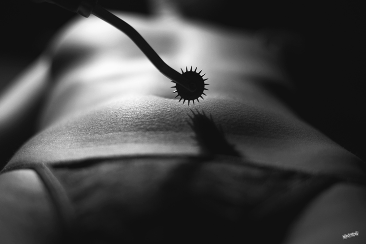 Kink. A rod with a round-shaped end with spikes coming out of it held near a nude woman's navel by someone not visible in the picture.