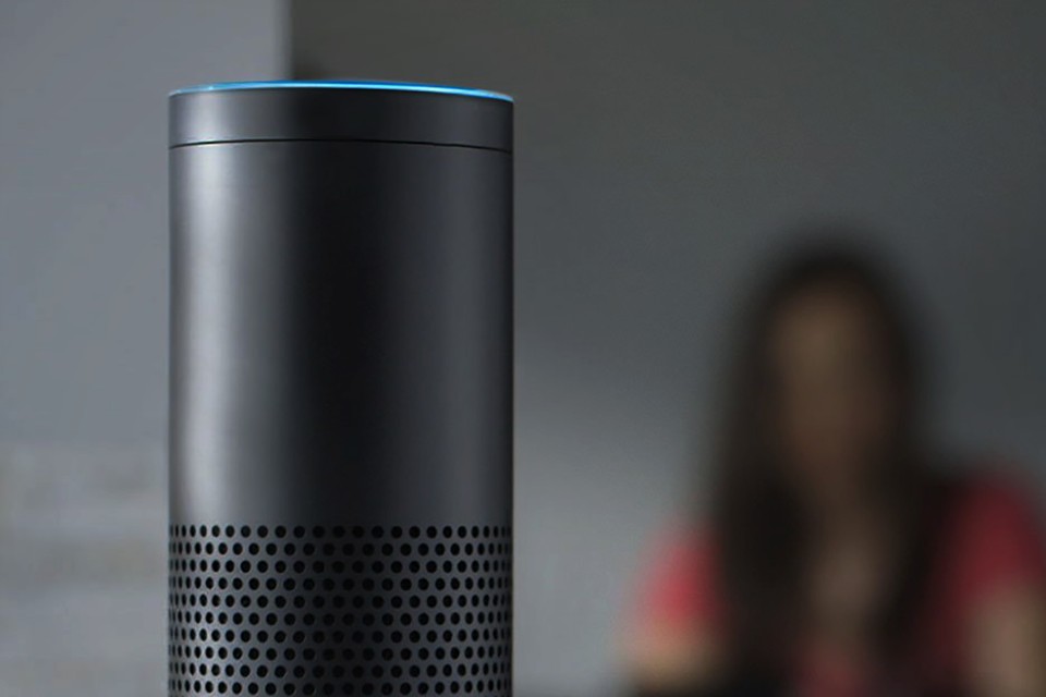 A closeup of a smart speaker by Amazon called Echo. Behind towards the right is a very blurred out woman. Screen reader support enabled. A closeup of a smart speaker by Amazon called Echo. Behind towards the right is a very blurred out woman.