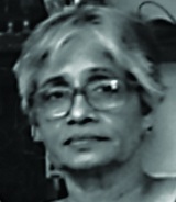 Black-and-white face-photo of Maya Sharma, middle-aged, white boy-cut hair, and is wearing specks.