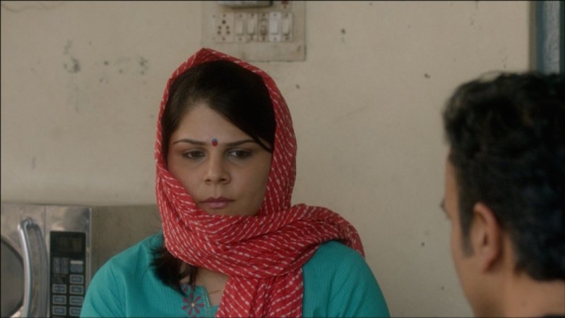 A woman looking down, wearing a green kurta and an aorange dupatta draped around her head