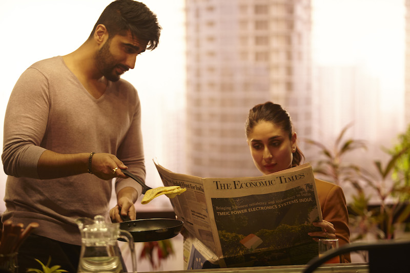 हिंदी फिल्म 'की एंड का' का एक दृश्य है, एक पुरुष और स्त्री, जो फिल्म में पति-पत्नी का किरदार निभा रहे हैं ।खाने की टेबल पर बैठी पत्नी अखबार पढ़ रही है और पति खाना परोस रहा है।