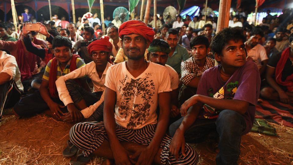 A photograph of a group of men sitting, where some of them are wearing a red cloth turban.