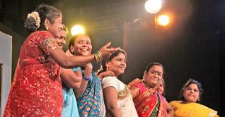 A photograph of a group pf women wearing sarees and speaking on the stage.