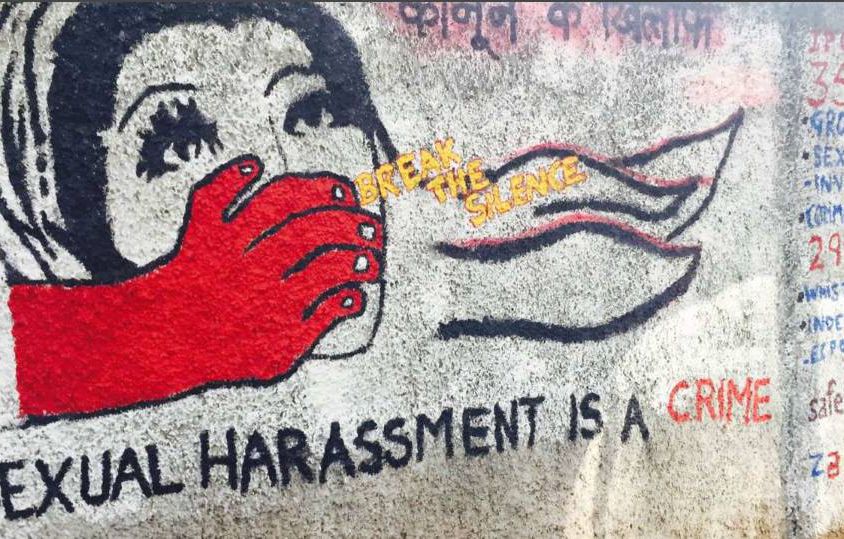 The photo shows a red hand trying to shut the mouth of a woman. There’s a caption on the photo saying sexual harassment is a crime and a yellow caption in between says, break the silence.