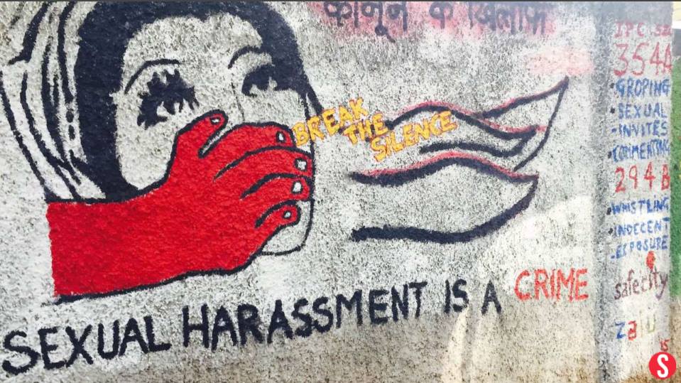 The photo shows a red hand trying to shut the mouth of a woman. There’s a caption on the photo saying sexual harassment is a crime and a yellow caption in between says, break the silence.