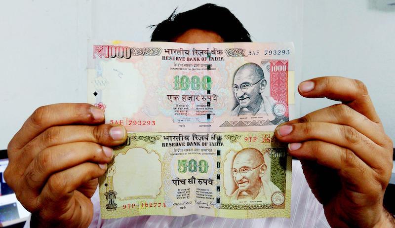 A photo of a man holding the old Rs.1000 and Rs.500 notes,