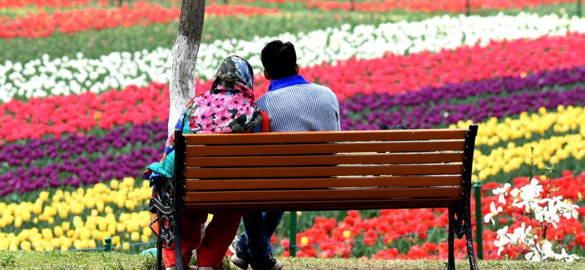 A young (Kashmiri) couple sitting on a bench facing backwards, looking at the garden.