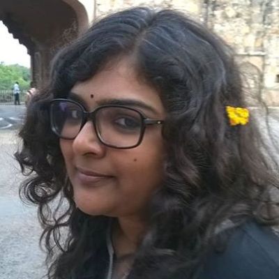 Its a selfie of the writer with open hair, wearing glasses, black bindi and a small yellow flower in her hair.