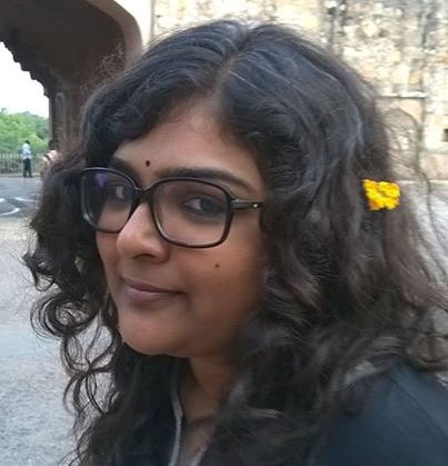 Its a selfie of the writer with open hair, wearing glasses, black bindi and a small yellow flower in her hair.