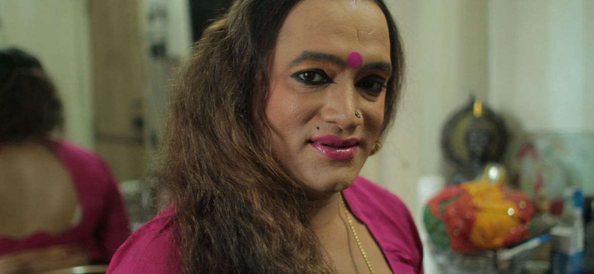 It's a still from the video, Laxmi, is smiling and wearing a pink bindi and saree, a silver nose pin. They have long hair, open in the photo and is wearing sindoor on their forehead.