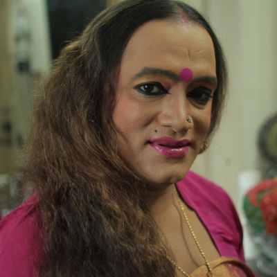 It's a still from the video, Laxmi, is smiling and wearing a pink bindi and saree, a silver nose pin. They have long hair, open in the photo and is wearing sindoor on their forehead.
