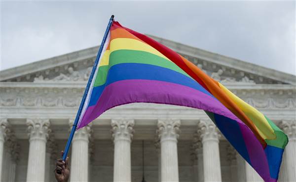 A brown hand holding the pride flag infront of the Whitehouse (in the background) . Screen reader support enabled. A brown hand holding the pride flag infront of the Whitehouse (in the background) .