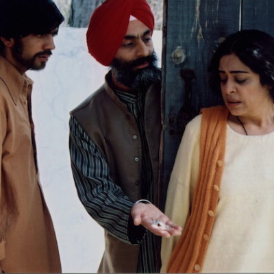 Its a still from the movie, Khamosh Pani,featuring Kirron Kher, standing with her back towards two men, one is a Sikh wearing a red turban offering something to the woman and the other man is looking towards them. Screen reader support enabled. Its a still from the movie, Khamosh Pani,featuring Kirron Kher, standing with her back towards two men, one is a Sikh wearing a red turban offering something to the woman and the other man is looking towards them.