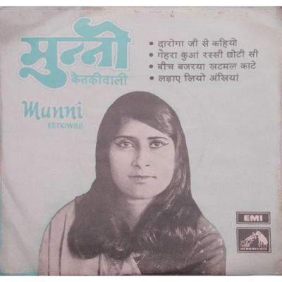 Its a poster of the singer, Munni Ketki Wali. Its in black and white, where a lady is smiling, wearing winged eye-liner, she has long hair. The caption on the poster says, मुन्नी केतकीवाली, Munni Kethkiwali and the names of her songs- दरोगा जी से कहिये गहरा कुआँ रस्सी छोटी सी बीच बज्रया खटमल काटे लढाये लियो अँखियाँ