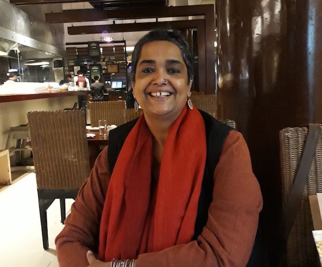 Picture of feminist activist Pramada Menon, she ihas short hair and is wearing a maroon kurta, black waistcoat and a red dupatta