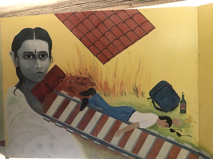 Art work shows a man lying on a railway line to commit suicide. A woman wearing a red bindi and a white saree stares straight ahead in grief.