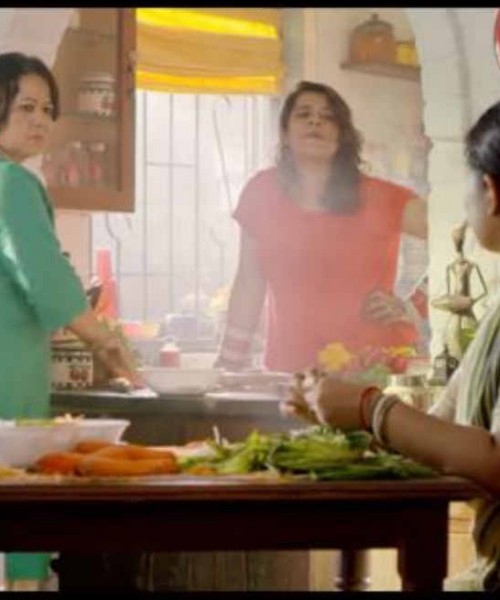 A still from a video. A mother, a daughter, and a maid are coversing while working in the kitchen.
