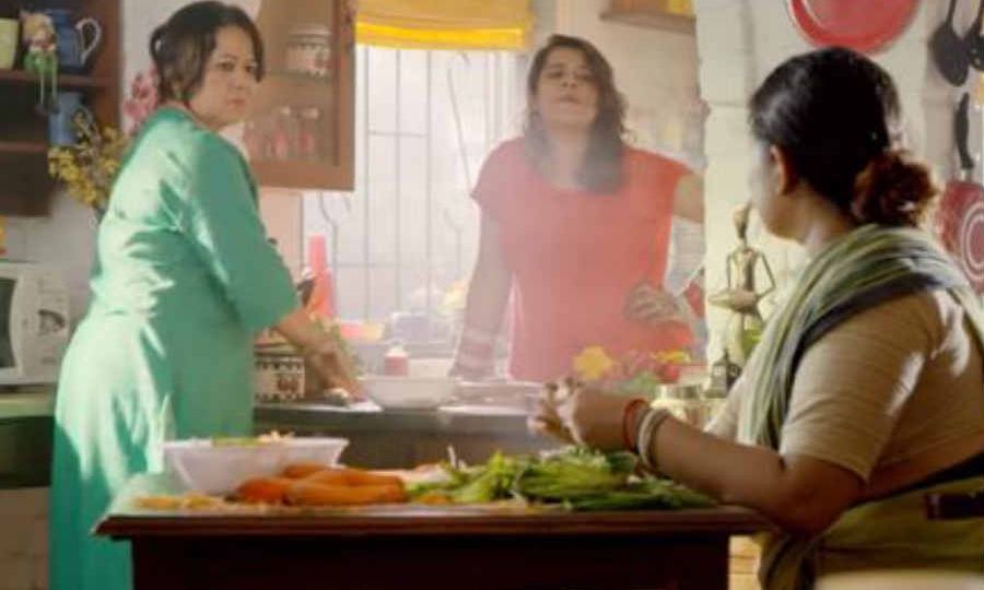 A still from a video. A mother, a daughter, and a maid are coversing while working in the kitchen.