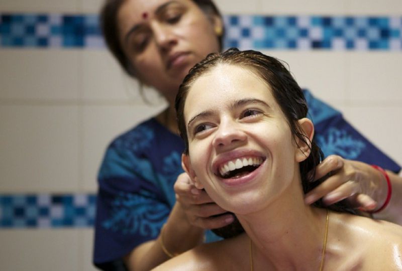 Still from an Hindi film "Margarita with a Straw". A young woman with oily hair is laughing. An older woman wearing a blue nightgown is massaging her hair.