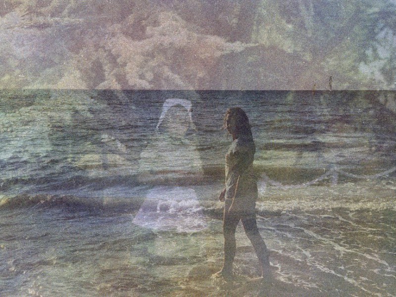 Two pictures are superimposed on each other. In the foreground is a picture of a woman standing on a beach. In the background is a picture of a little girl staring straight at us.