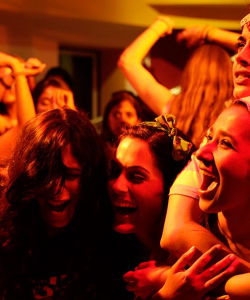 Scene from a Hindi movie 'Angry Indian Goddesses'. The six protagonists are standing together laughing, in a disco with bright lighting.