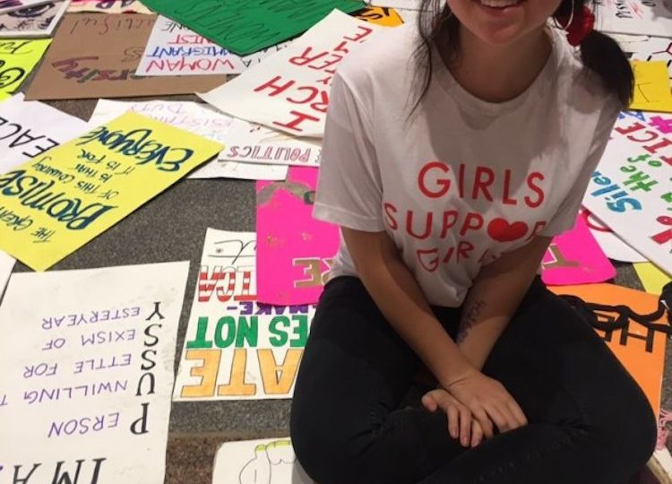 Photo of art student Emma Krenzer. She is dressed in a white t-shirt and black trousers, with her hair tied in a ponytail.