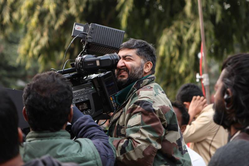 Photo of trans activist and cinematographer Satya Rai Nagpaul, holding up a camera to shoot a film