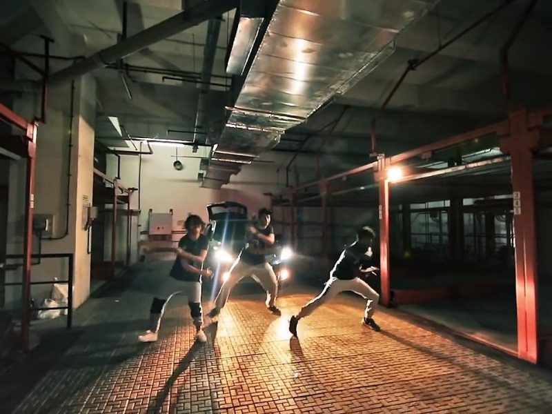A still from a music video, showing a bunch of men dancing on the street.