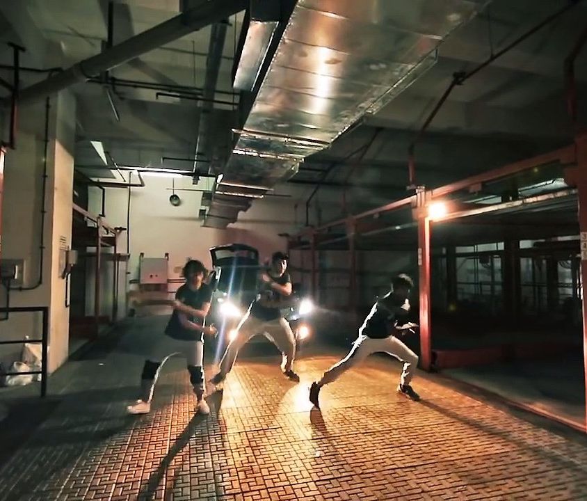 A still from a music video, showing a bunch of men dancing on the street.