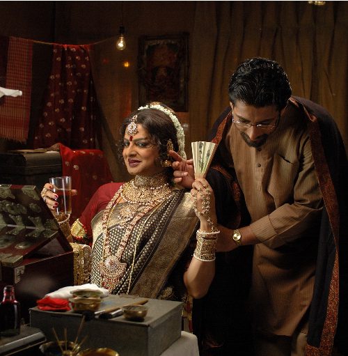 Still from the film: Arekti Premer Golpo, showing a man crossdressed as a woman, wearing a cotton sareer, red blouse, and gold jewellery