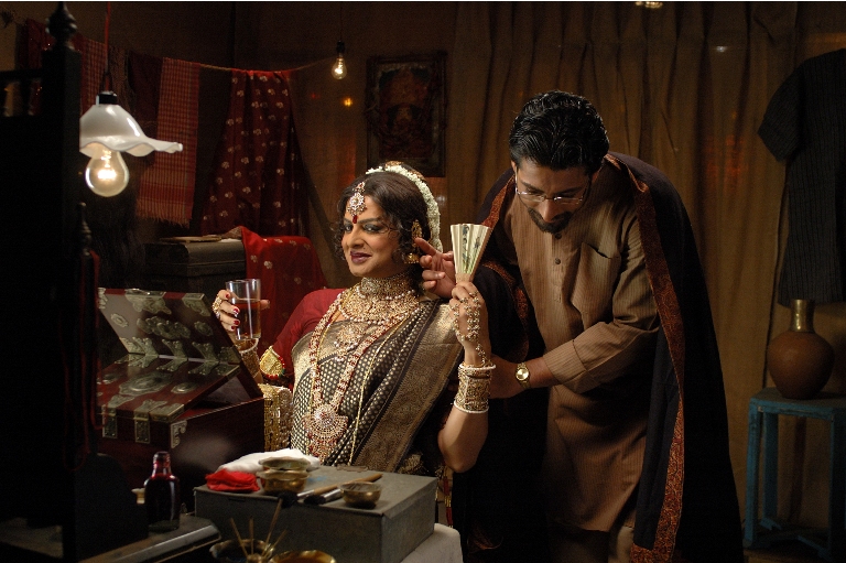 Still from the film: Arekti Premer Golpo, showing a man crossdressed as a woman, wearing a cotton sareer, red blouse, and gold jewellery