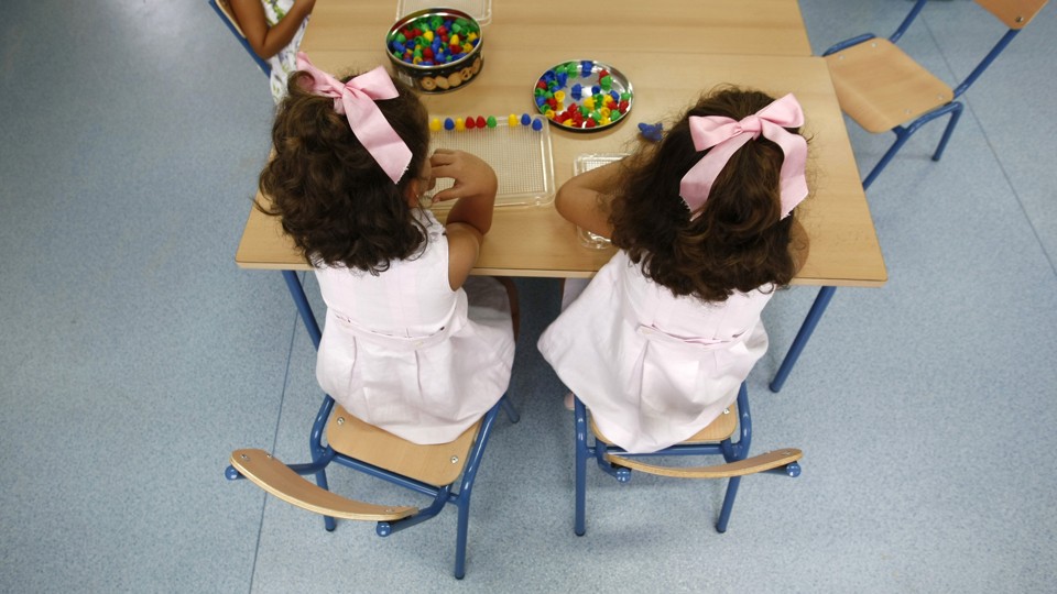 An image of two little girls sitting at a table, facing their backs to the camera. Marcelo del Pozo / Reuters