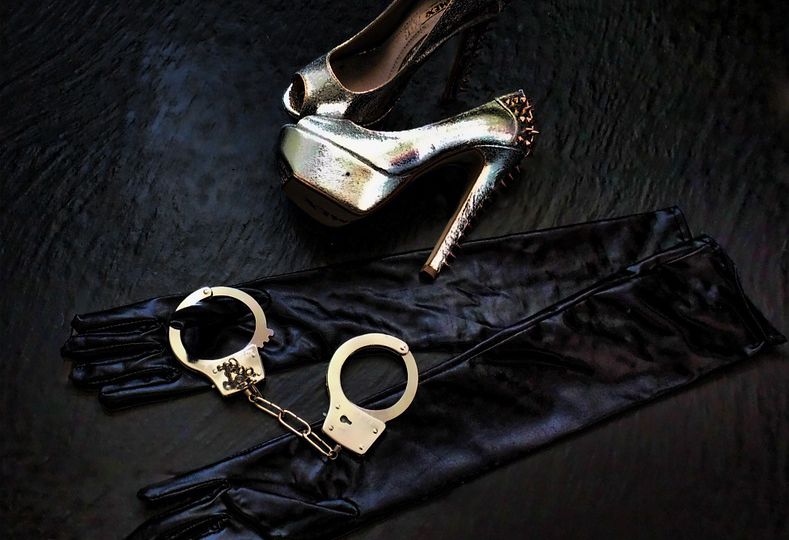 Picture of a pair of heels and a steel handcuffs , along with black silk gloves lying on the floor