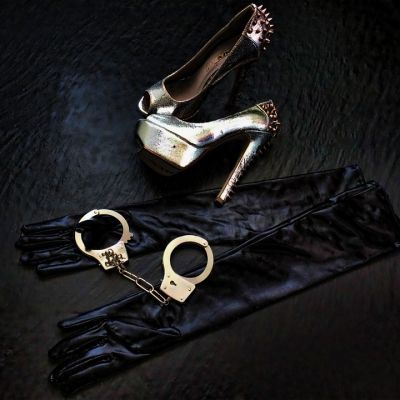 Picture of a pair of heels and a steel handcuffs , along with black silk gloves lying on the floor
