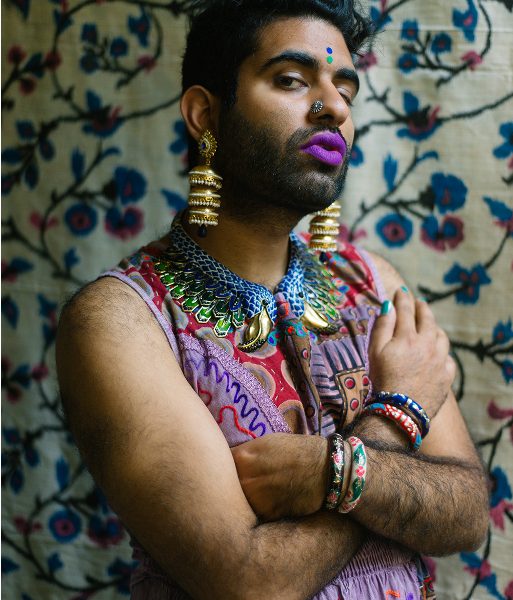 Gender non-conforming poet Alok Vaid Menon. They are dressed in a vibrant sleeveless dress, jewellery and makeup.